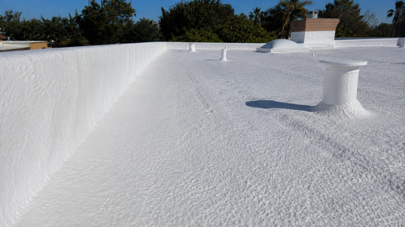 Close view of a seamless coating running up a parapet wall and around a vent