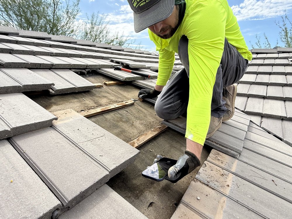 Roofer on a concrete tile roof with tiles lifted aside, exposing the wood battens and underlayment beneath