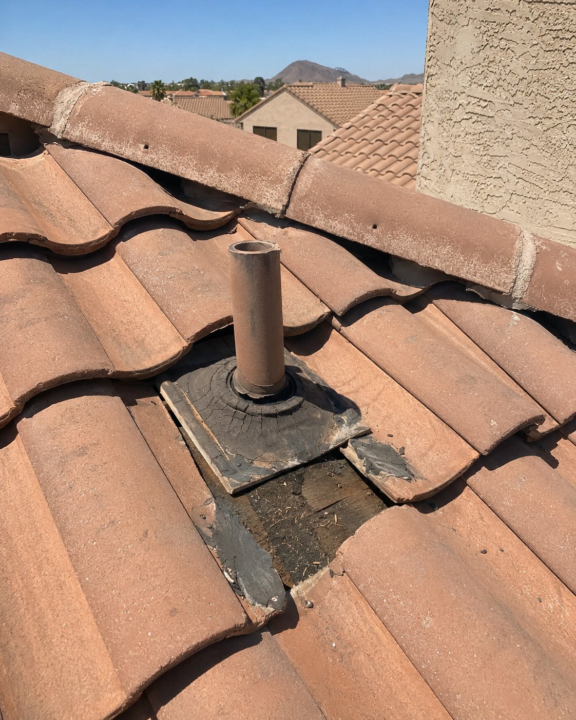 A cracked and deteriorated lead pipe boot on a barrel tile roof, with tiles pulled back and exposed decking