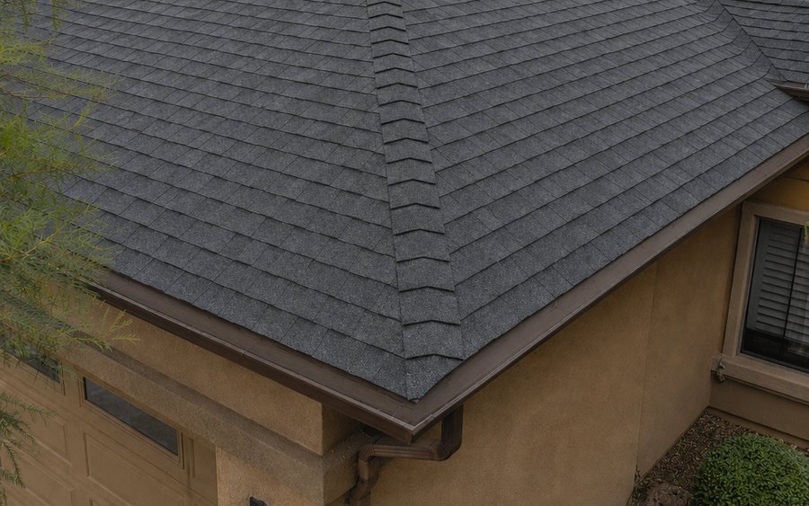 Gutter running along the eave of a shingle roof against a stucco wall