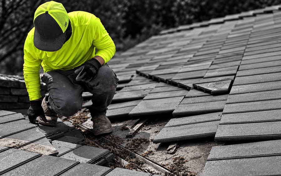 Roofer crouched among broken and displaced concrete tiles, clearing debris from the course beneath
